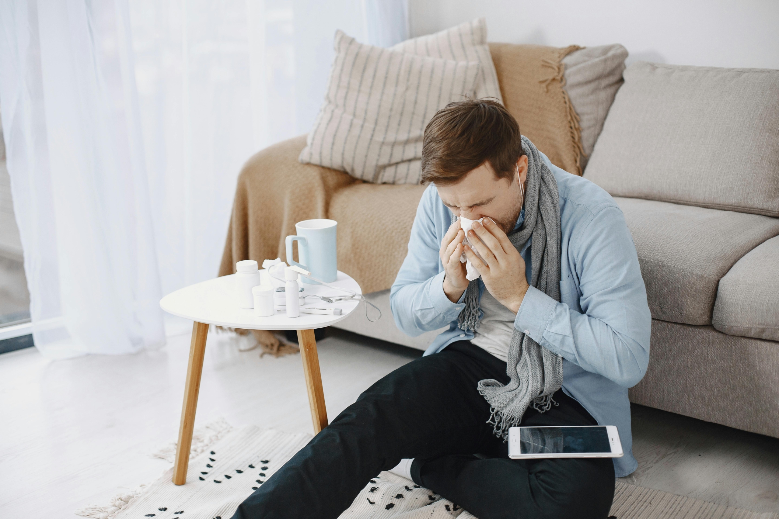 Man sneezing at home in the Philadelphia area next to his allergy medications